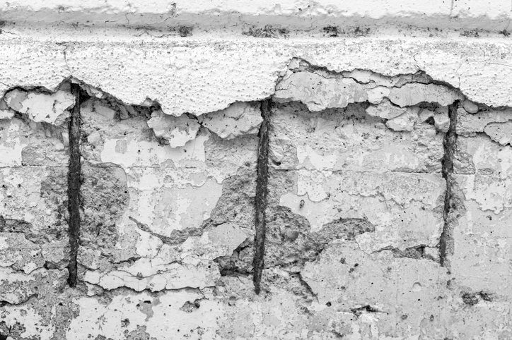 Concrete cancer with exposed rusting reinforcement bars and spalling render on a concrete wall